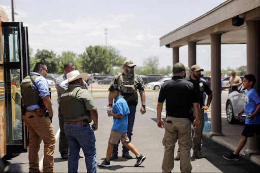 Students exit Robb Elementary in Uvalde, and are guided onto buses by law enforcement .